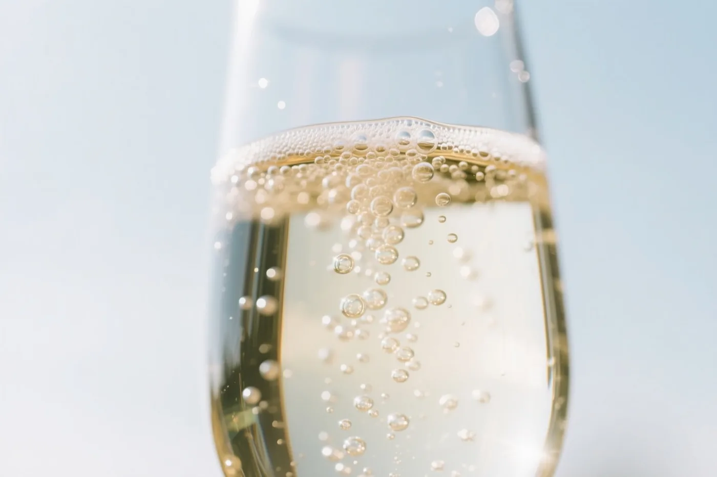 Een close-up toont mousserende wijn met opstijgende belletjes in een glas voor een zachte onscherpe lichtblauwe achtergrond.