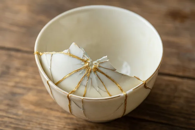 Een witte keramieken kop met een stervormige barst die met gouden lijnen is hersteld, staat op een houten tafel.