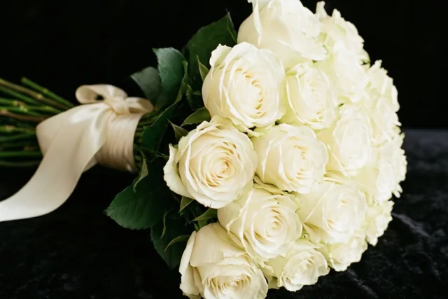 Een boeket witte rozen met een ivoorkleurig satijnen lint ligt op zwart fluweel.