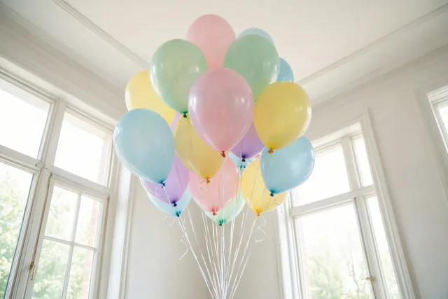 Een tros zachtroze, gele, lichtblauwe en mintgroene ballonnen zweeft in een lichte, luchtige kamer met hoge ramen.