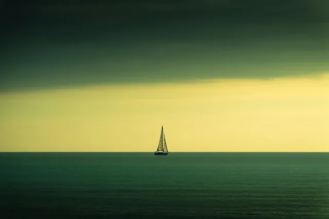 Een eenzame zeilboot is zichtbaar aan de horizon van een kalme zee onder een hemel met kleurverloop, in groene en gele tinten.