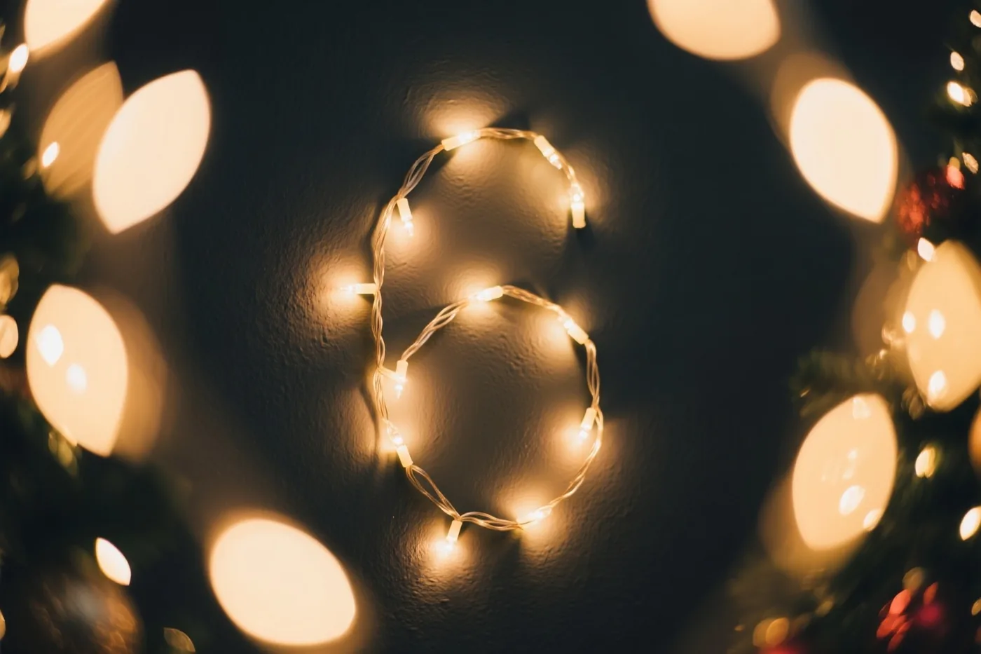 Warme lichtjes vormen het cijfer 6 op een donkere muur met structuur, met onscherpe feestlichtjes errond.